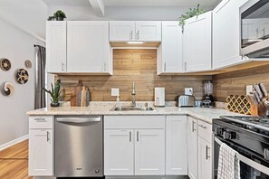 Een moderne keuken met witte kasten, roestvrijstalen apparatuur en een houten spatwand.