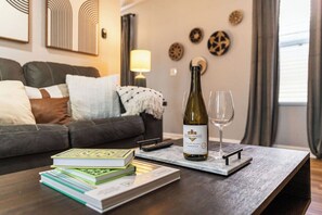 Een zithoek met een donker leren bank, een salontafel met boeken en een wijnfles, en een lamp op de achtergrond.