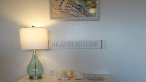 Een wit bureau met een lamp, een bordje met de tekst 'Beach House' en een schilderij erboven.