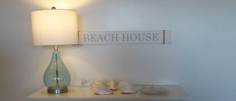 A desk with a lamp, a 'BEACH HOUSE' sign, and a painting above.