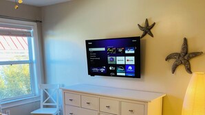 Een slaapkamer met een bed, een aan de muur bevestigde televisie, decoraties met zeesterren en een lamp.