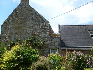 Un bâtiment en pierre avec un toit en pente, une fenêtre et un vélo garé à l’extérieur.