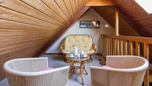 Une pièce mansardée chaleureuse, avec des lambris en bois, un fauteuil à motifs floraux, des chaises en osier et une petite table sur laquelle est disposé un service à thé.