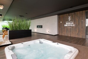 A modern indoor spa area with a hot tub, wooden flooring, and a wall-mounted TV. - Modern Apartment | Spa Area | Close to the Beach (Kolobrzeg)