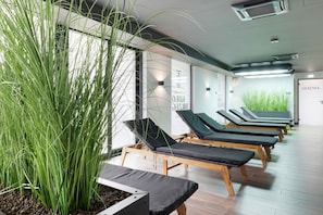 Une salle de spa moderne avec des chaises longues en bois, une grande plante en pot et un mur orné de texte.