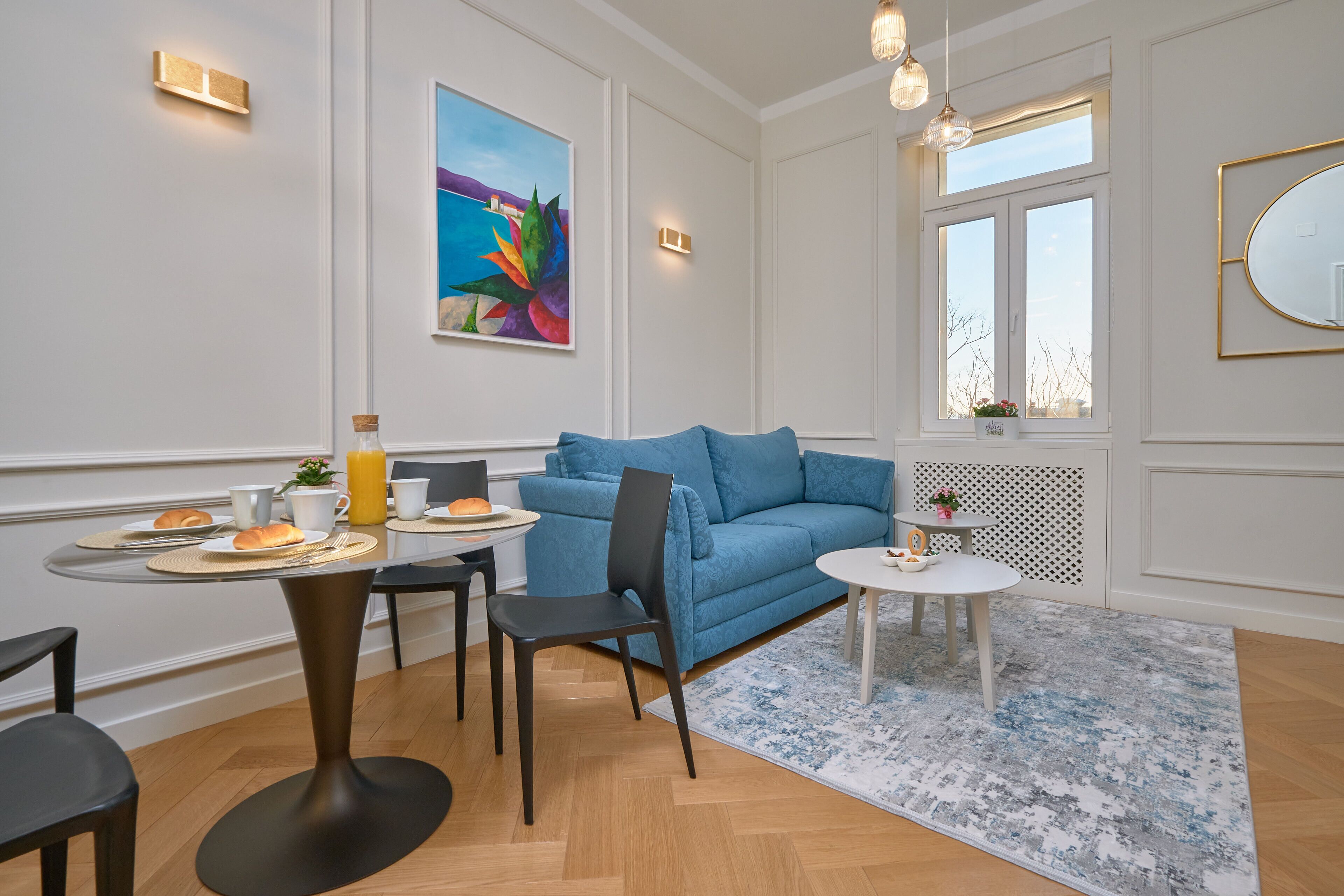 Ein modernes Wohnzimmer mit einem blauen Sofa, einem Esstisch mit Frühstücksgebäck und einem großen Fenster mit Blick.