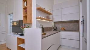 A modern kitchen with white cabinetry, wooden shelves, and a built-in TV. - Salve Luxury Apartment by Litto (Split)