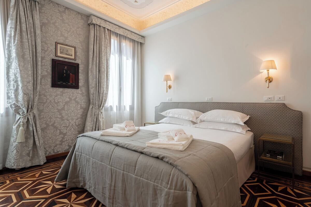 A hotel room with a large bed, two bedside lamps, a nightstand, and a patterned floor.