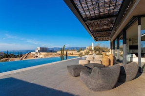Un espace piscine extérieur moderne offrant une vue dégagée sur la mer et les montagnes en arrière-plan.