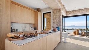 Een moderne keuken met houten kastjes, een marmeren aanrechtblad en uitzicht op zee.