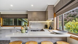 A modern kitchen with a large island, bar stools, and a view of a garden. - Lumeah Retreat Adventure Bay, Bruny Island (Adventure Bay)