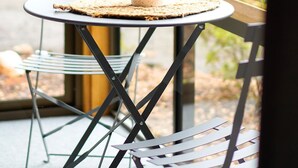 A round table with a woven placemat, a potted plant, and two metal chairs with a cross-back design. - Lumeah Retreat Adventure Bay, Bruny Island (Adventure Bay)