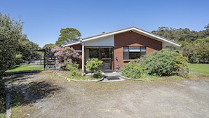 A modern two-story house with a brick facade, a large garage door, and a well-maintained garden with various plants and shrubs. - Lumeah Retreat Adventure Bay, Bruny Island (Adventure Bay)