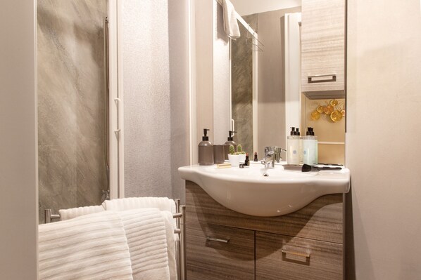 A modern bathroom with a curved sink, a large mirror, and a towel rack. - Fair Suite (Rome)