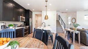 A modern kitchen with dark cabinets, a central island, and a dining area with a wooden table and chairs.