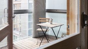 Uma varanda com mesa e cadeira de madeira, uma caneca branca e vista para edifícios.