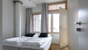 Um quarto com uma cama, uma janela, uma porta e chão de madeira.