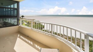 Un balcon donnant sur la plage, avec une balustrade blanche et une porte vitrée qui mène à l’intérieur.