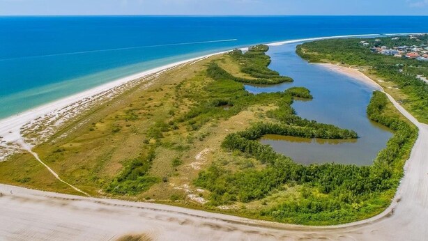Vue aérienne d’une zone côtière comprenant une plage, une voie navigable et un petit village.