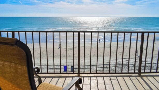 Una terraza de madera con barandilla de metal que da a una playa.