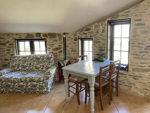 Un comedor con una mesa blanca y sillas de madera, un sofá floral y paredes de piedra.