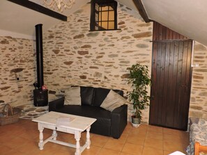 Un ambiente acogedor con pared de piedra, sofá negro, mesa blanca, planta en maceta y puerta de madera.