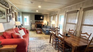 A living room with a red sofa, a wooden dining table, and a television. - Humble Heaven - Beachfront - Island Realty (Grand Isle)