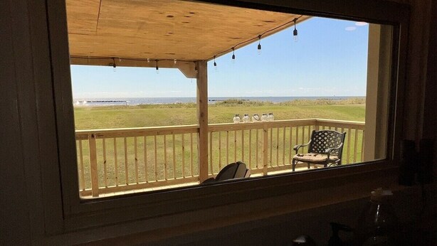 A room with a large window overlooking a grassy deck with a chair. - Humble Heaven - Beachfront - Island Realty (Grand Isle)
