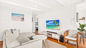 A modern living room with a grey sofa, a round coffee table, a TV on the wall, and a wooden chair. - Cape Surf House in Cape Woolamai (Cape Woolamai)