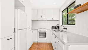 A compact kitchen with white cabinetry, a built-in oven, a stove, and a sink. - Cape Surf House in Cape Woolamai (Cape Woolamai)