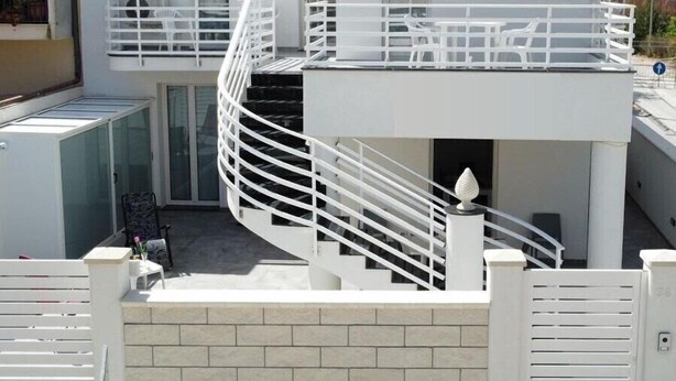 Een modern gebouw met twee verdiepingen, een witte gevel en een spiraaltrap. Een bordje geeft 'THE HOUSE' aan.
