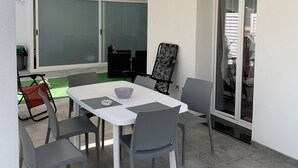 Een terras met een tafel en stoelen, een witte parasol en een schuifdeur van glas.