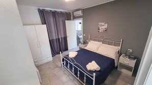 Een slaapkamer met een bed, nachtkastje, kledingkast en een raam met gordijnen.