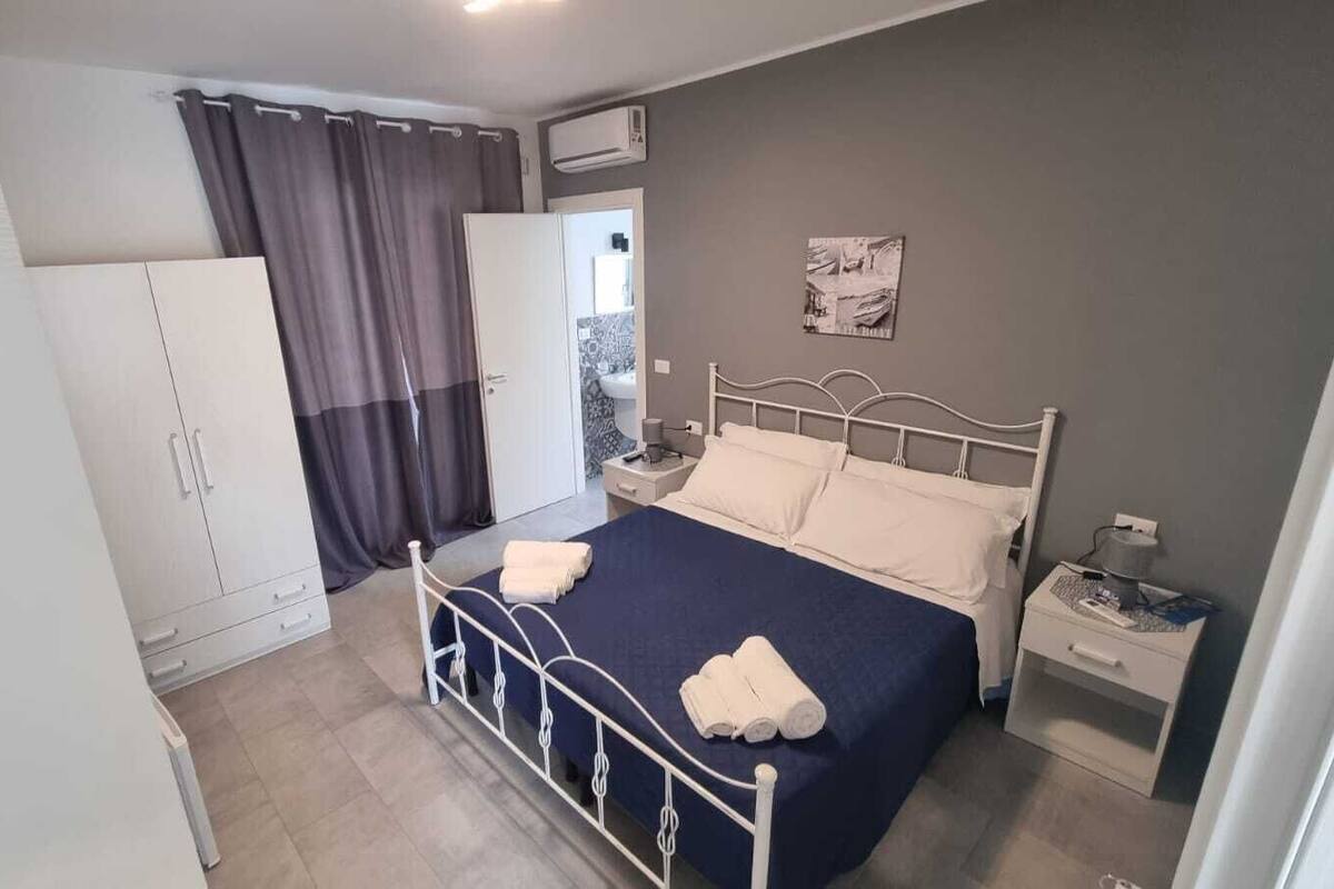 Een slaapkamer met een bed, nachtkastje, kledingkast en een raam met gordijnen.