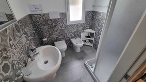 Een badkamer met een wastafel, toilet, bidet en een klein plankje met toiletartikelen.