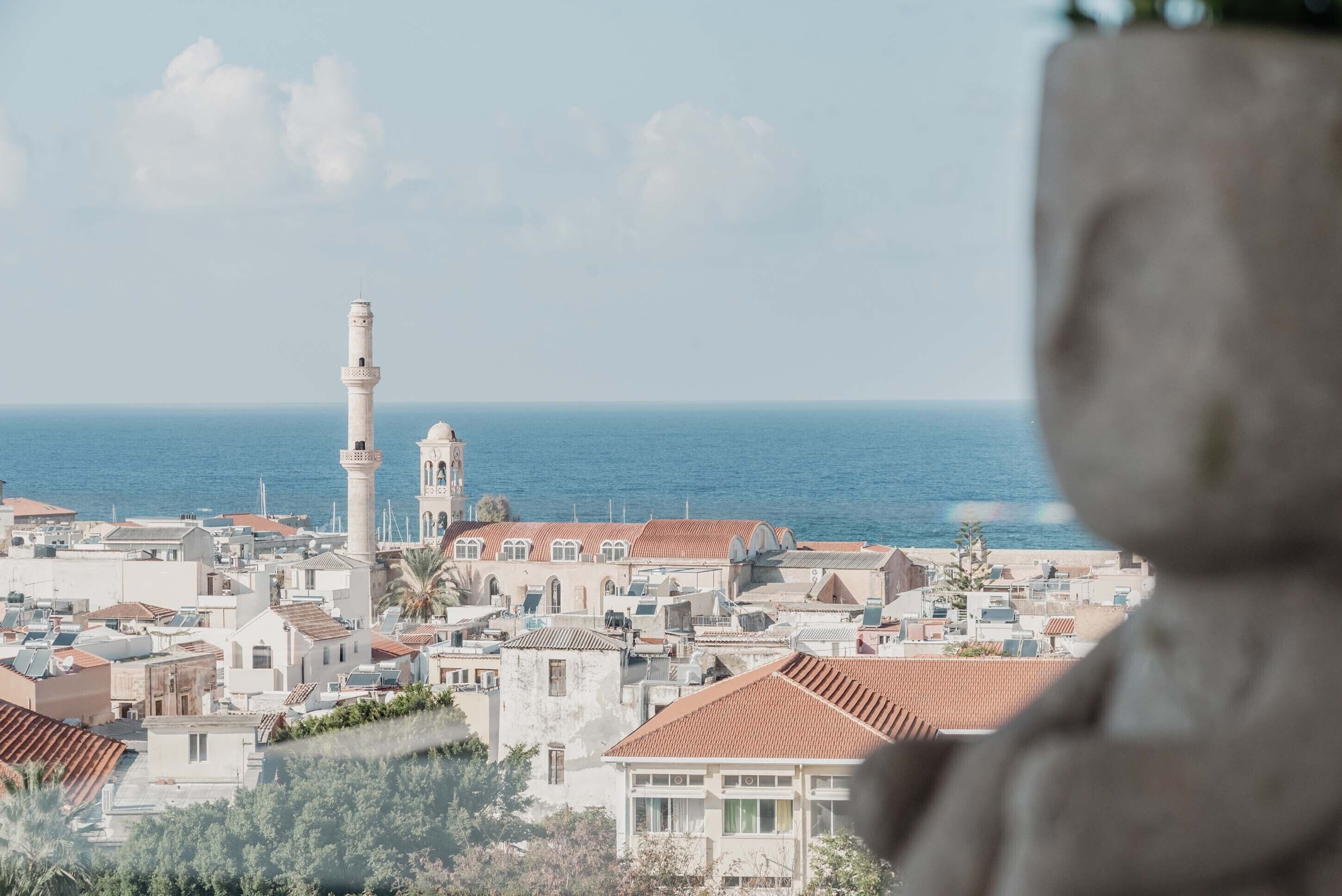 A coastal town with a prominent white tower, terraced buildings, and a view of the sea.