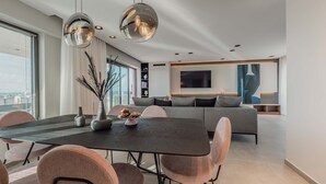 Un salon moderne avec un coin repas, un canapé gris et un téléviseur fixé au mur.