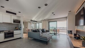 Un salon moderne avec un canapé gris, un coin repas et une cuisine équipée d’appareils électroménagers intégrés.