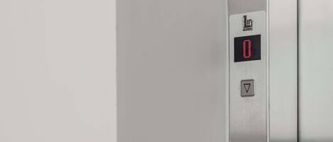 A metallic elevator control panel with a digital display showing '0' and a downward-pointing arrow.