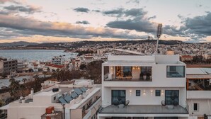 Un bâtiment moderne doté d’une terrasse sur le toit, d’une grande fenêtre et offrant une vue sur la mer et le paysage urbain.