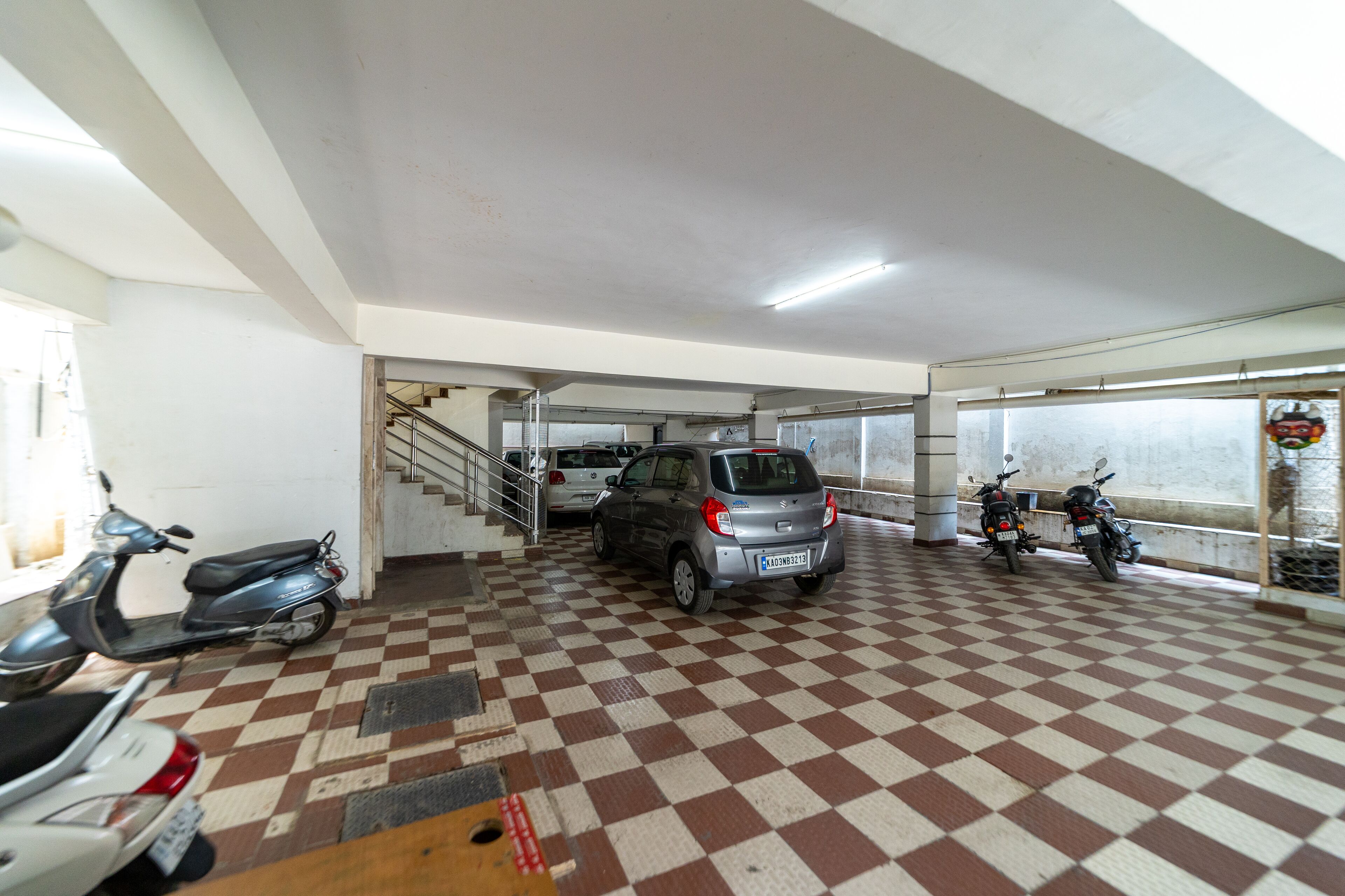 A parking area with a checkered floor, a staircase, and several parked vehicles including scooters and a car.