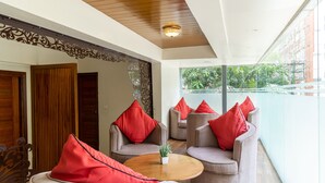 A modern interior with a round wooden table, grey sofas with red cushions, and a view of greenery outside. - Tetrad Hotel - International Airport Road Hebbal (Bengaluru)
