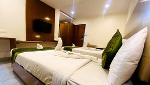 A hotel room with a large bed, a flat-screen TV mounted on the wall, and a wooden wardrobe. - Tetrad Hotel - International Airport Road Hebbal (Bengaluru)