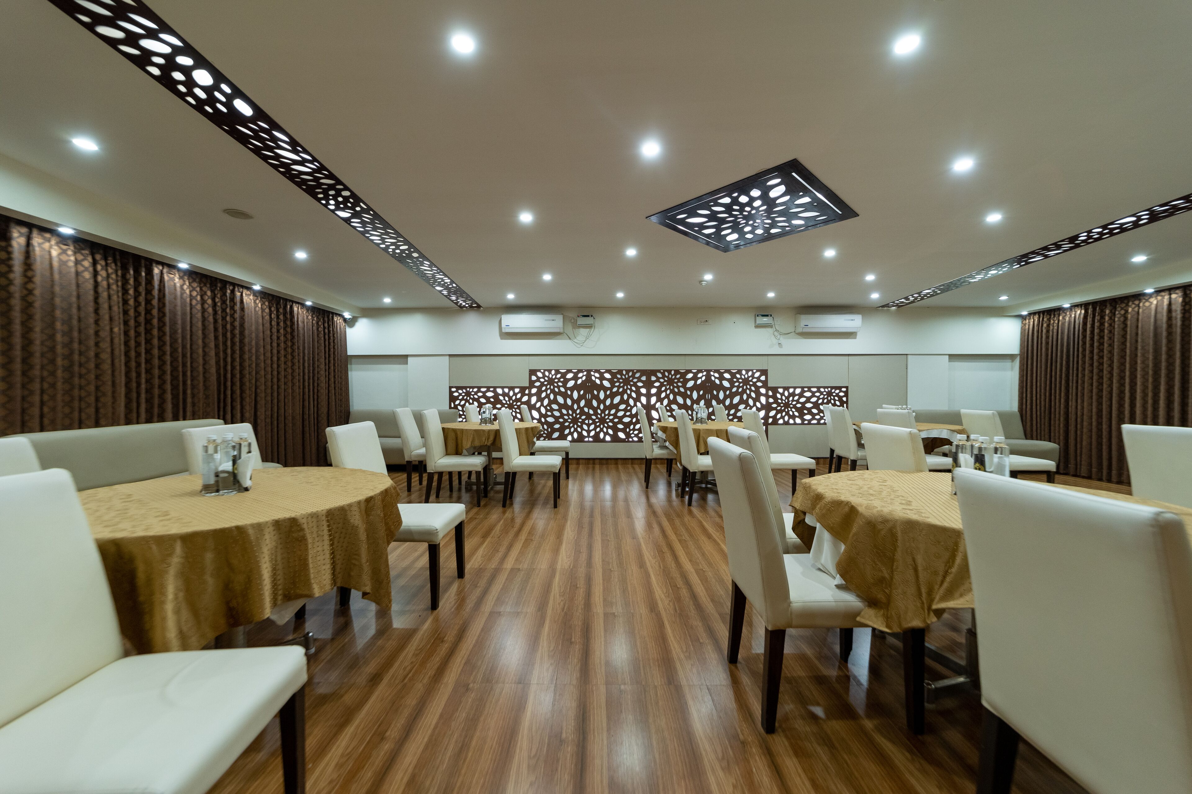 A dining area with round tables, white chairs, and a decorative wall with cut-out patterns.
