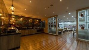 A modern hotel lobby with wooden flooring, a reception desk, and a dining area with tables and chairs. - Tetrad Hotel - International Airport Road Hebbal (Bengaluru)