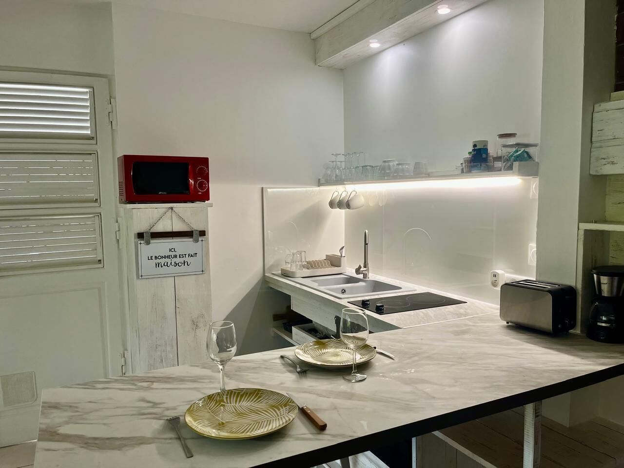 A modern kitchen with a marble countertop, a toaster, a coffee maker, and a wine glass on the table.