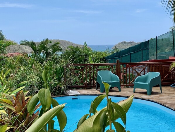 Ein Poolbereich mit zwei türkisblauen Liegen, umgeben von üppiger Vegetation und Blick aufs Meer.