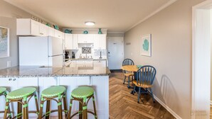 Eine moderne Küche mit weißen Schränken, einer Marmorarbeitsplatte und einem Essbereich mit einem Holztisch und blauen Stühlen.
