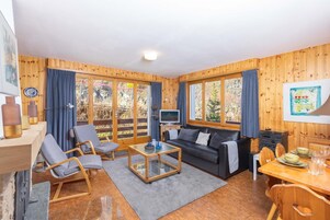 A cozy cabin interior with wooden walls, a sofa, a coffee table, and a dining area.