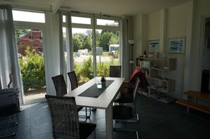 Enjoy meals at the large dining table surrounded by comfortable chairs, with a sliding door leading to a garden view.